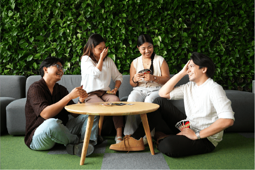 group of colleagues sharing a light, friendly conversation around a coffee table in a relaxed lounge