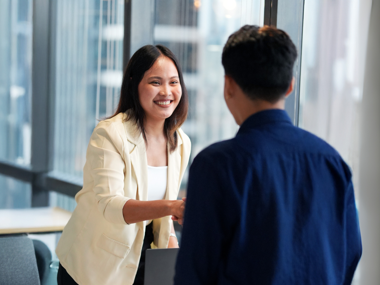 A professional lady in cream-coloured blazer shaking hands with a businessman in the office